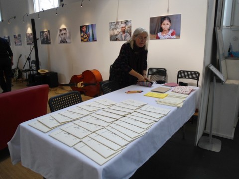 A long table with white cloth lined with copies of the pamphlet. At one end, Annie is bent over the table organising something. 