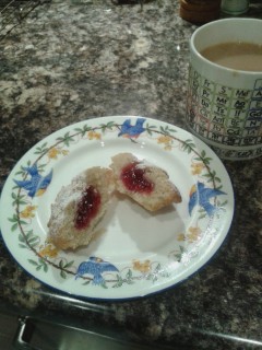 Mug of tea, and china plate with raspberry bun cut open to reveal red jam inside